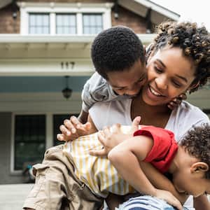 Young mother playing with two sons in front of house 